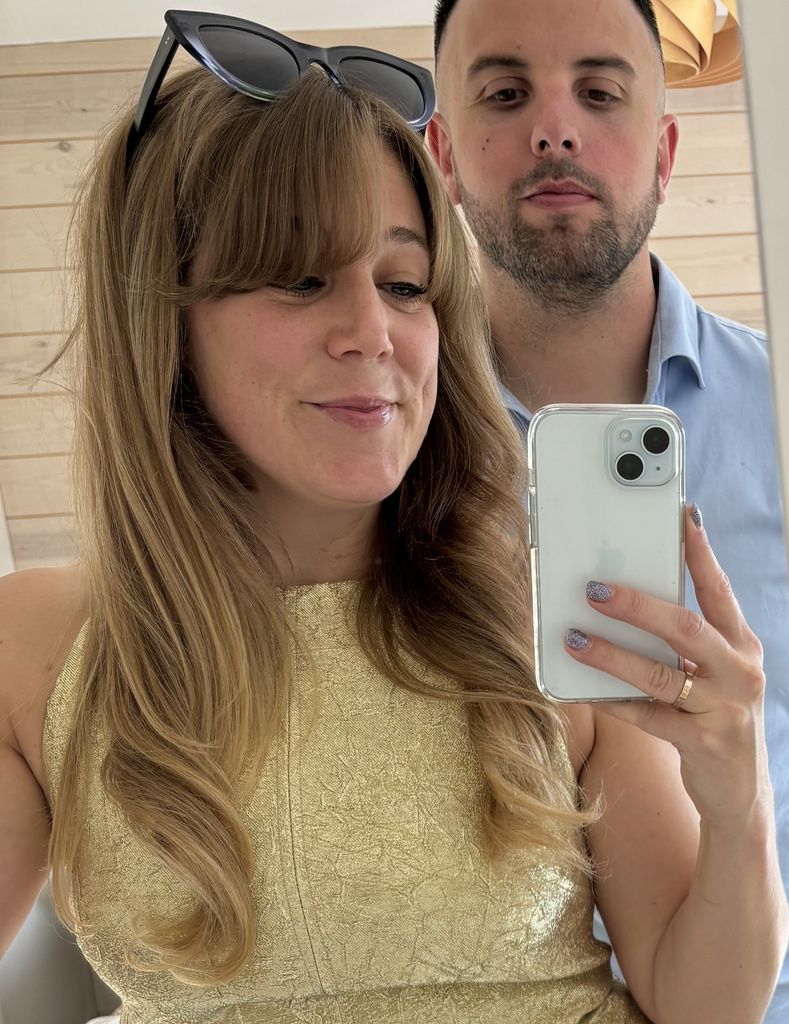 blonde woman in a gold dress taking a selfie with a friend behind