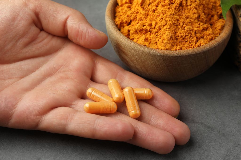 Woman with turmeric pills and aromatic powder at grey table, closeup