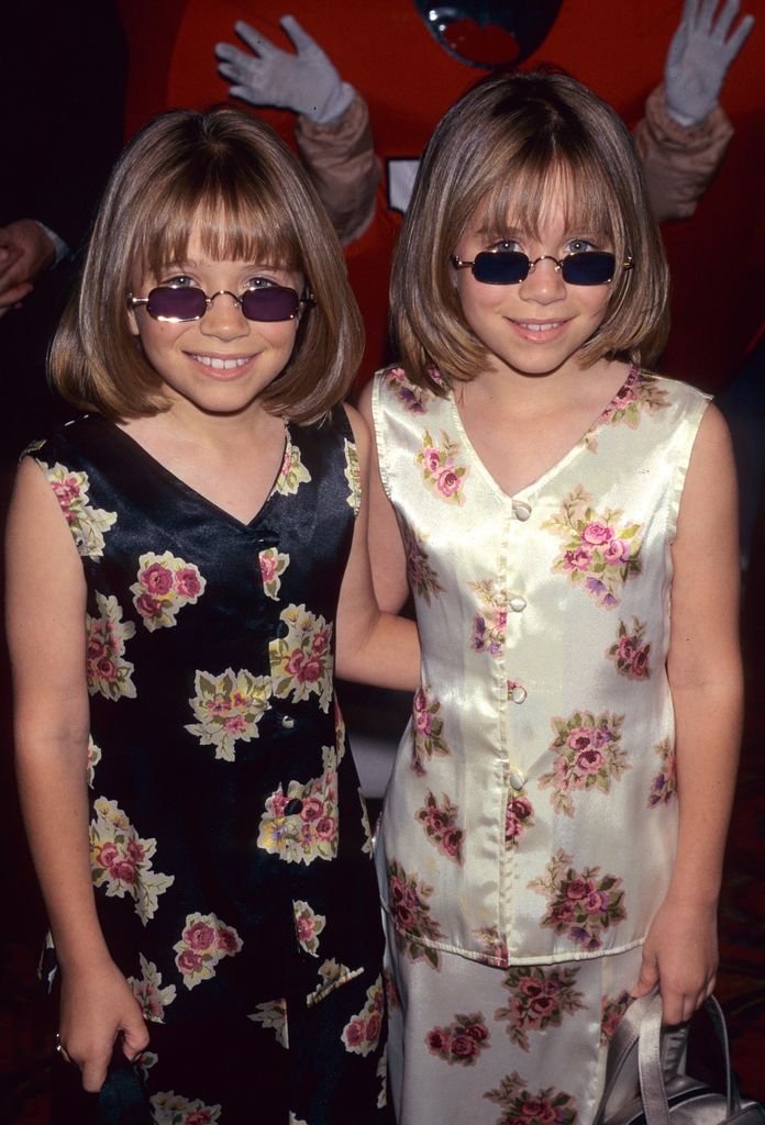 Mary-Kate Olsen and Ashley Olsen stood together in floral dresses wearing sunglasses