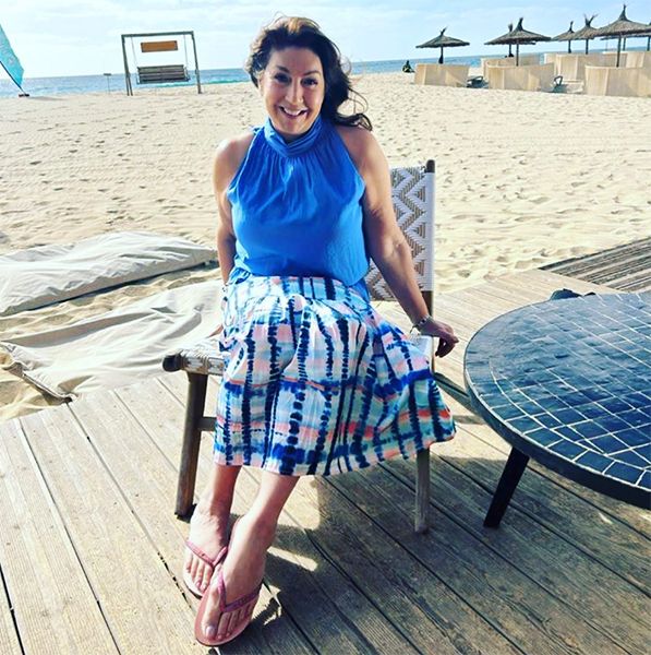 Jane McDonald on the beach in blue shirt and skirt