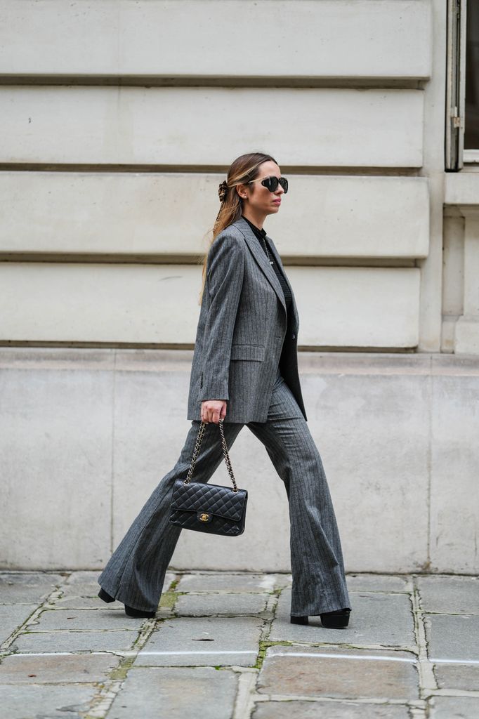 Maria Rosaria Rizzo wears a grey pinstripe suit by Ungaro Paris, black Saint Laurent sunglasses and a black quilted Chanel bag in Paris.