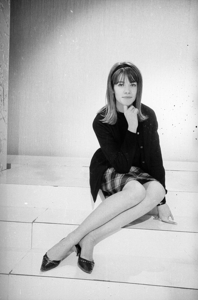 Francoise Hardy poses in a plaid mini skirt, black sweater and pointed flats, exuding 60s mod chic during Eurovision 1963.