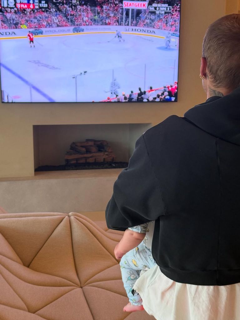 Photo of Justin Bieber from behind watching TV with his baby son on his lap