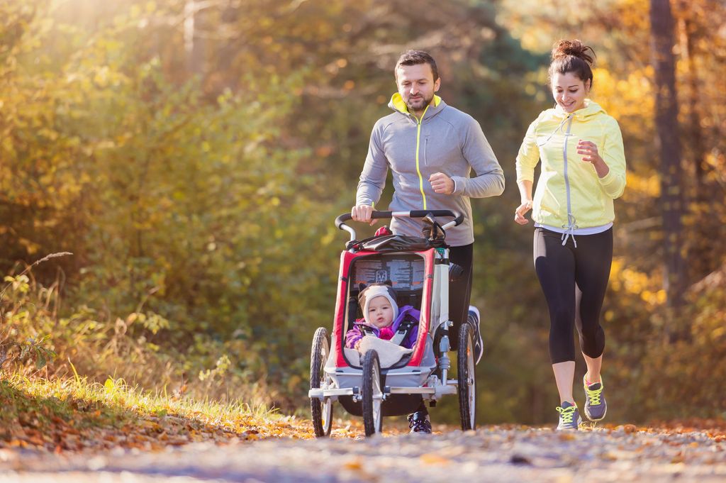 Young family with baby in jogging stroller running outside 