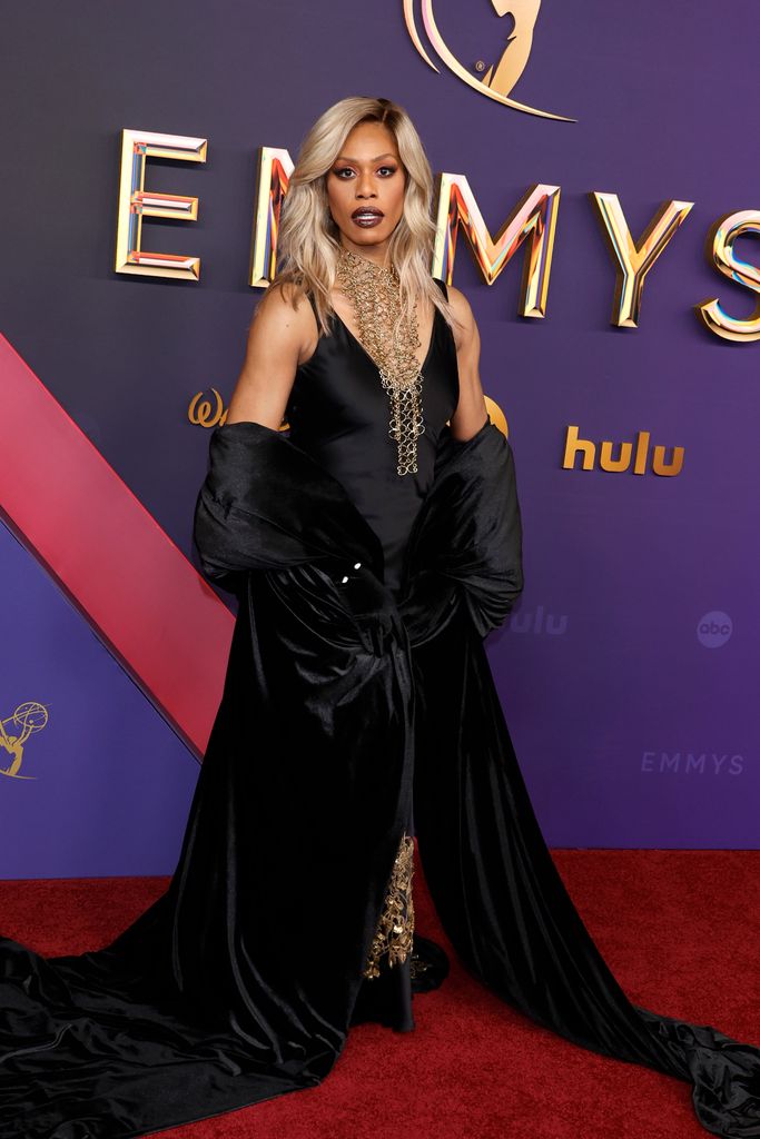 Laverne Cox dazzles in a black gown with a plunging neckline, adorned with a dramatic gold chain necklace.