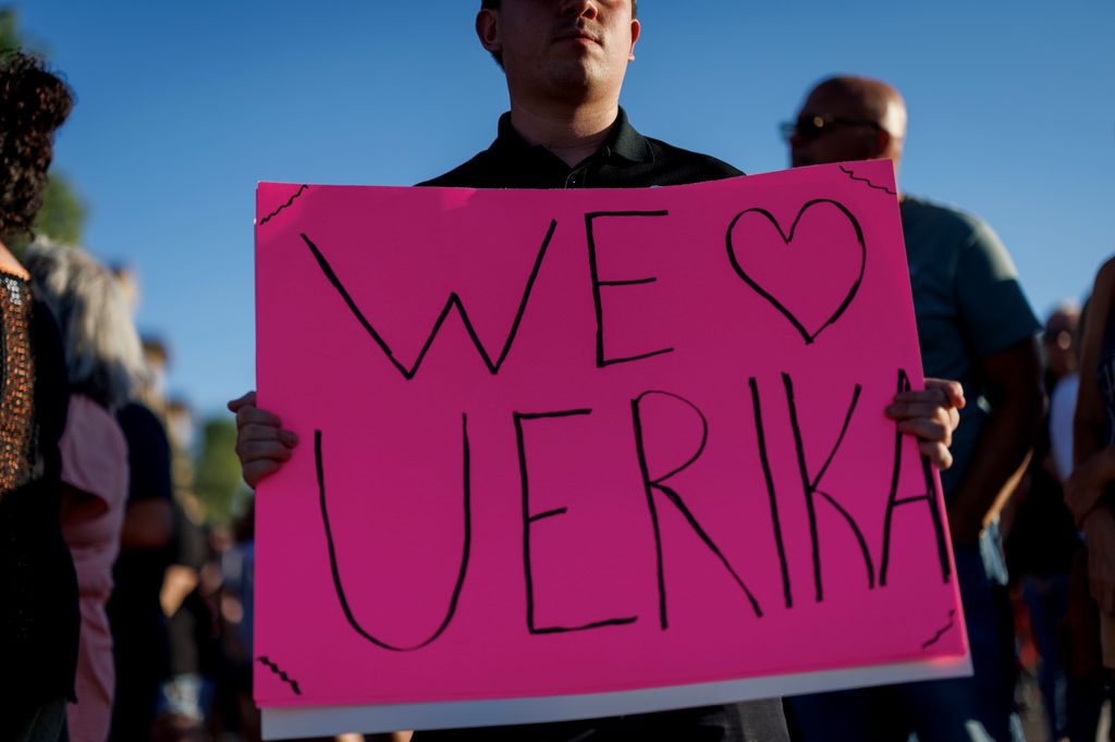 A man holds a sign saying 'we love u Erika'