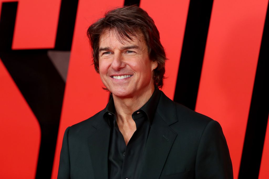 Tom Cruise in a black suit smiles on red carpet 