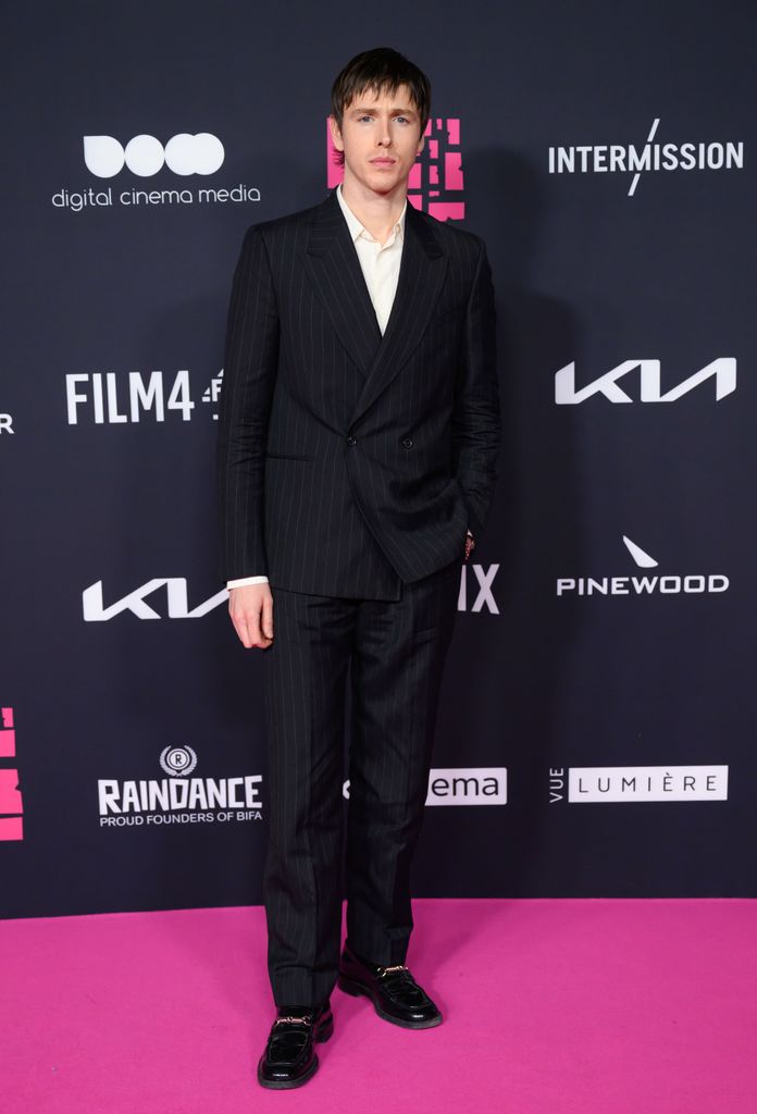 Harris Dickinson on pink carpet in black suit
