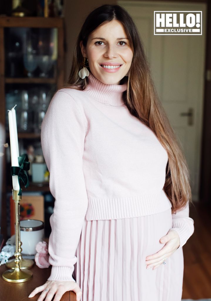 Manon in a pink outfit holding her baby bump