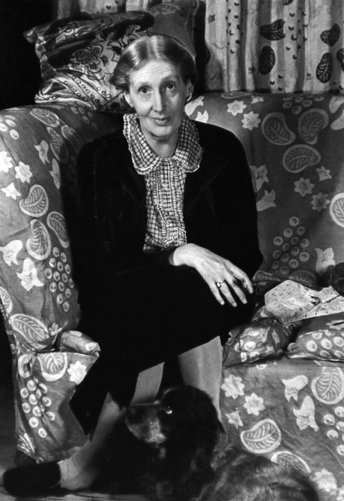 Portrait of English author Virginia Woolf (1882 - 1941) as she sits cross-legged on a couch, with her Cocker Spaniel, Pinka, at her feet, London, England, 1939.