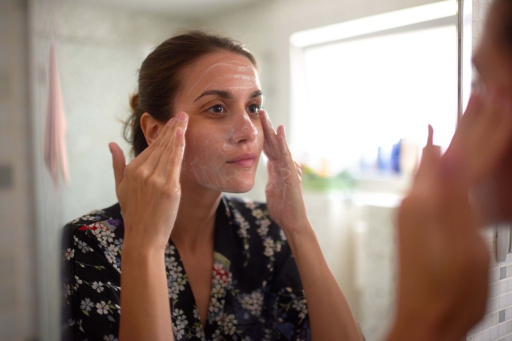female in the bathroom looking in the mirror and taking care of her facial skin by applying facial cream.