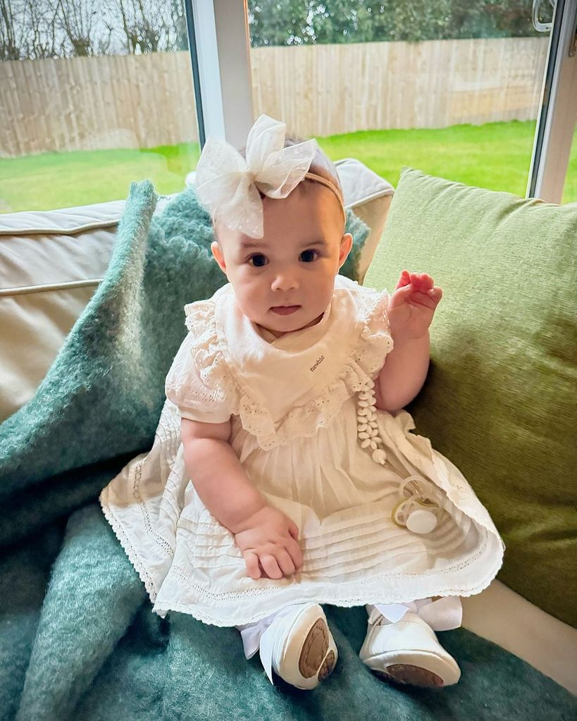Janette Manrara's daughter Lyra in a white ruffled dress on the sofa