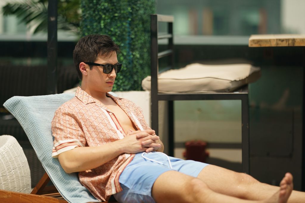 Hudson Williams as Shane Hollander sitting by a swimming pool in an open shirt