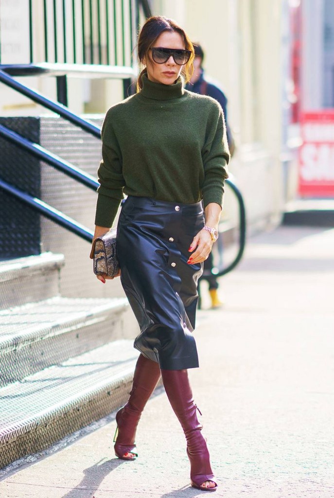 Victoria Beckham wears a leather midi skirt, green sweater and burgundy boots