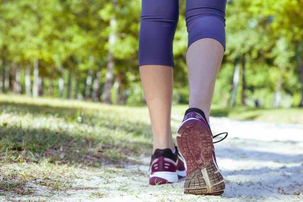 Close-up of a woman's legs in purple leggings walking on a dirt trail in sports sneakers.