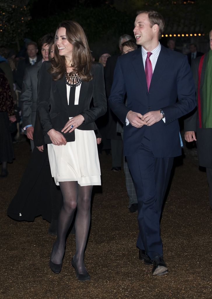 Kate in white mini dress with a black blazer and black pumps beside william in suit laughing