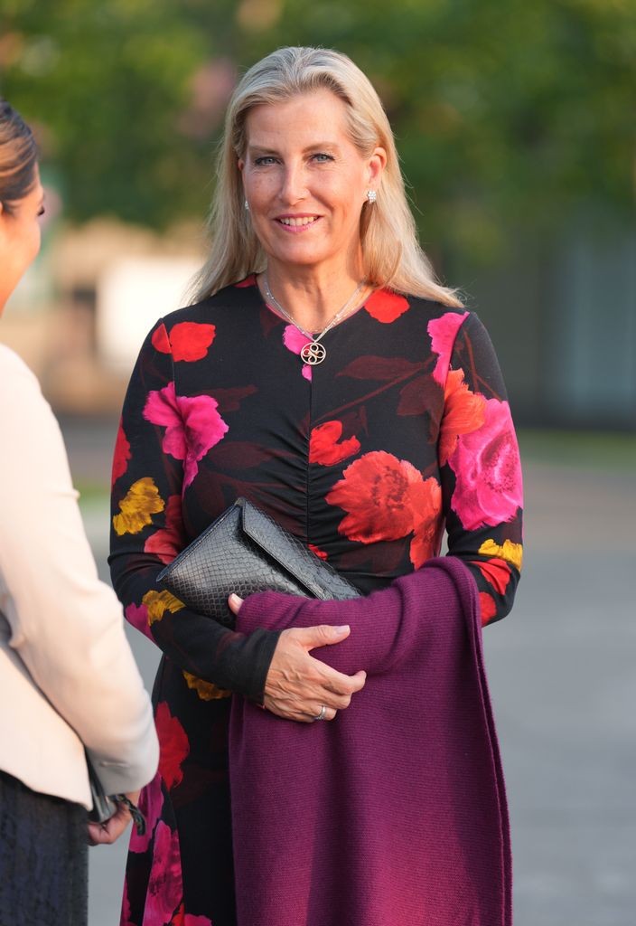 The Duchess of Edinburgh in black and red floral dress talking to woman