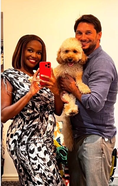 Pregnant Oti Mabuse in bodycon dress and husband Marius Iepure posing with dog