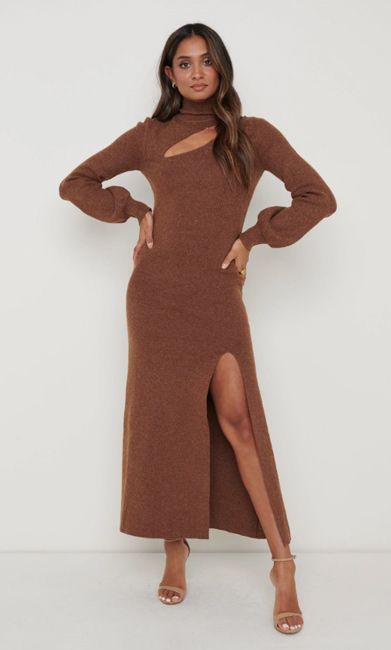 a fashion model wears a fitted brown dress featuring a cut out design on the chest and a thigh split against a pale backdrop