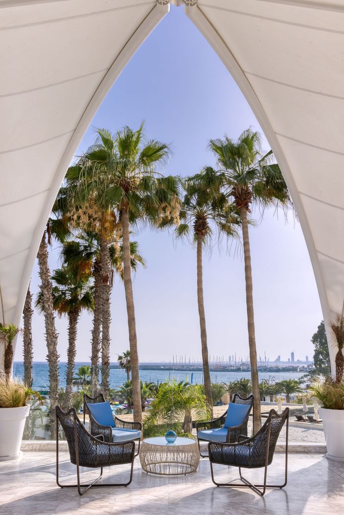 Four chairs and a table under and archway with palm trees in the background