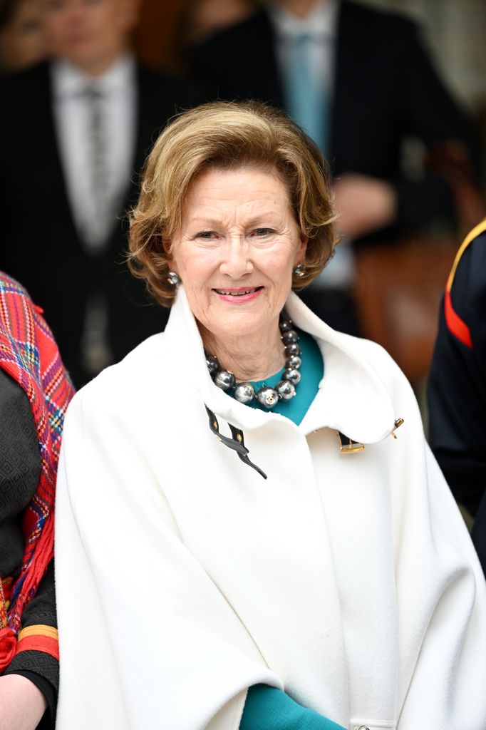 Queen Sonja wearing cream coat and chunky necklace