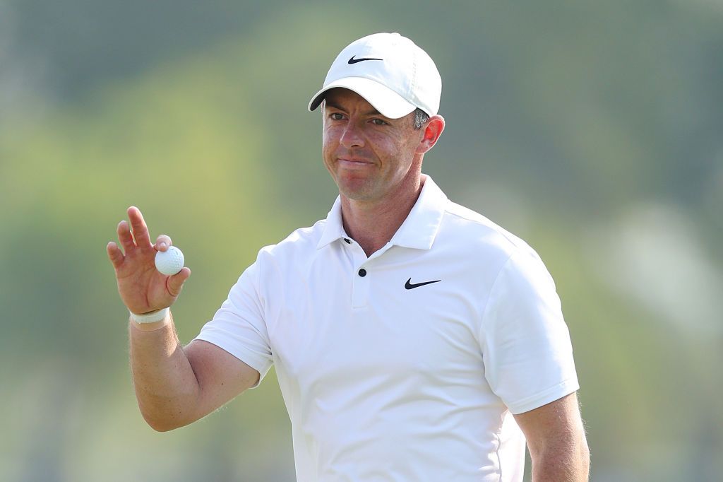 Rory McIIroy dressed in white wearing a hat and holding up a golf ball