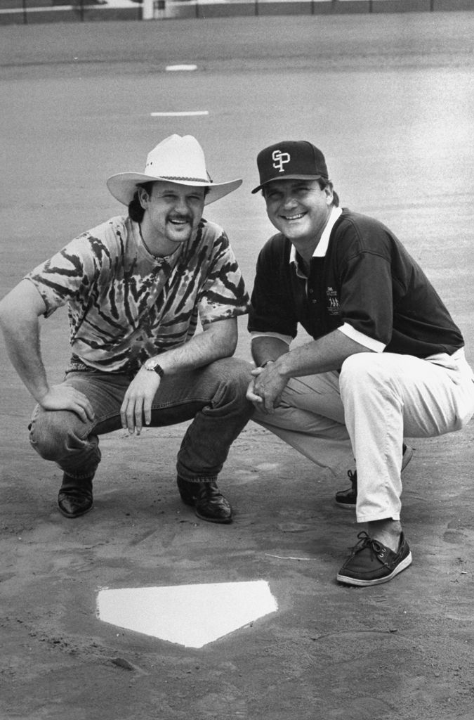 C&W musician Tim McGraw w. father, former baseball player Tug McGraw in baseball cap, as they crouch next to home plate on baseball field.