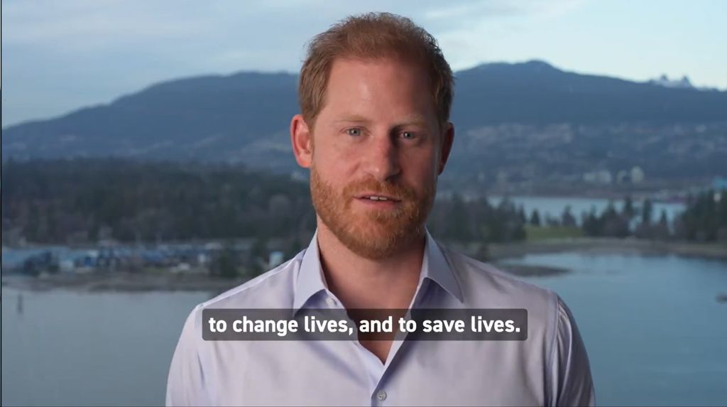 Prince Harry in a blue shirt in front of a lake and forest