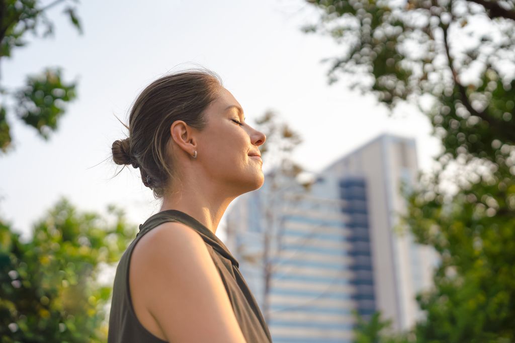 Businesswoman taking a break in urban park, enjoying the gentle breeze with her eyes closed.