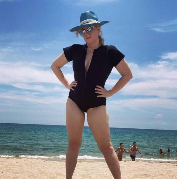 Rebel Wilson poses on the beach in a black zip-up swimsuit