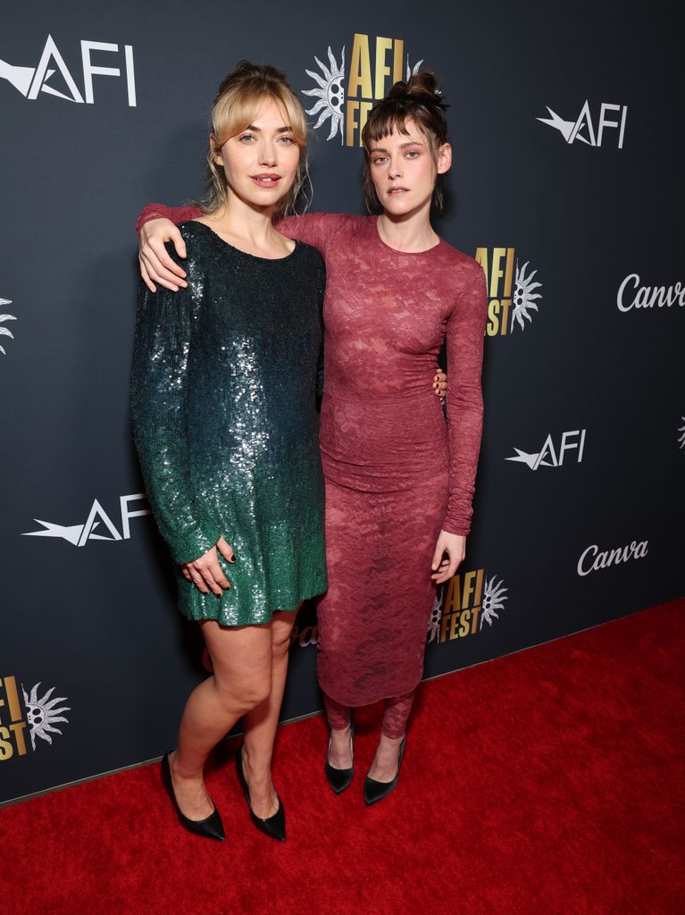 Imogen Poots wears a green ombre sequin mini dress with black heels and stands next to Kristen Stewart in her sheer burgundy dress. Kristen has her arm around Imogen's shoulders. 
