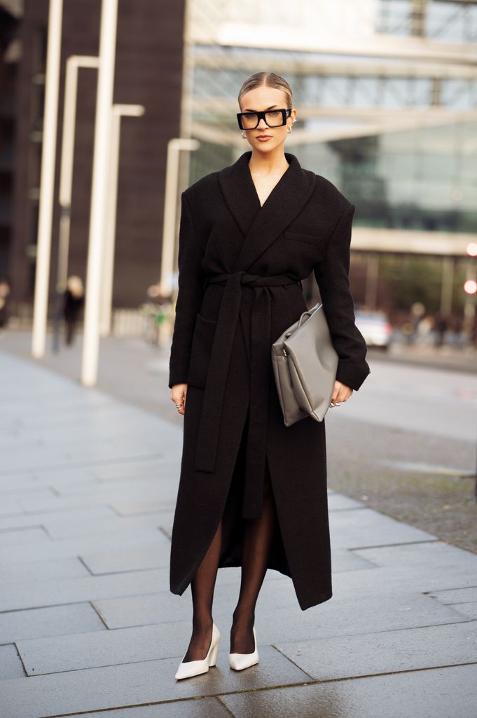 Emilia Silberg wears long black coat, black tights, white pointy shoes, grey bag and statement glasses outside the OpÃ©raSport show during the Copenhagen Fashion Week Autumn/Winter 2025 on January 27, 2025 in Copenhagen, Denmark.