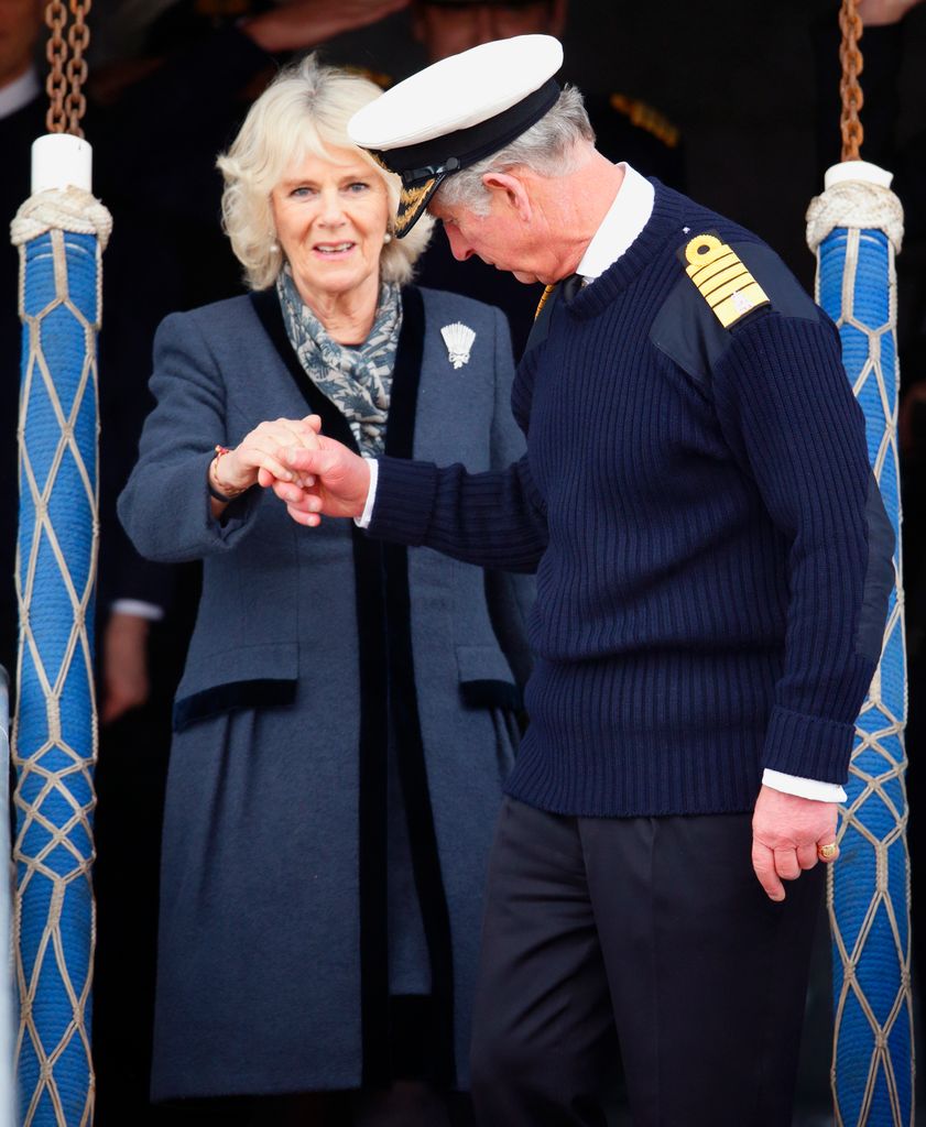 Charles holds Camilla's hand as they disembark HMS Illustrious