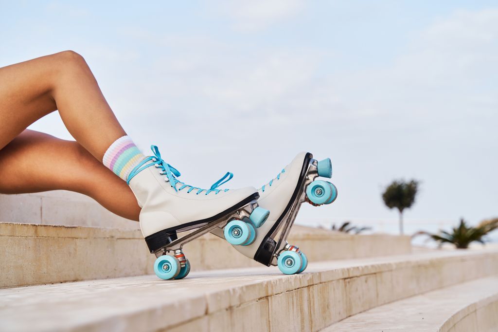 Side view of crop anonymous female in striped socks and fashionable retro style white quad roller skates with blue laces and wheels sitting on the steps on urban seafront