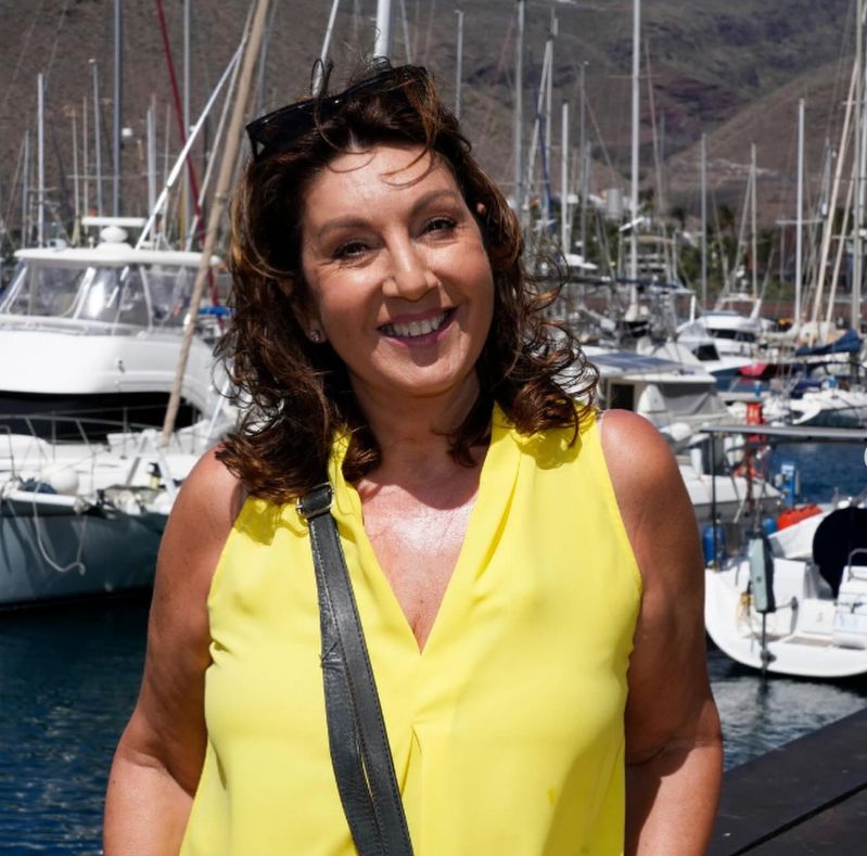 Jane McDonald in a yellow outfit in front of several boats