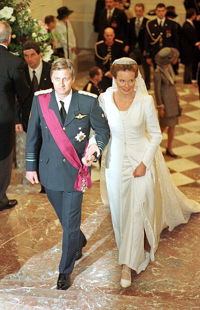 King Philippe of Belgium in a suit linking arms with Queen Mathilde in her wedding dress