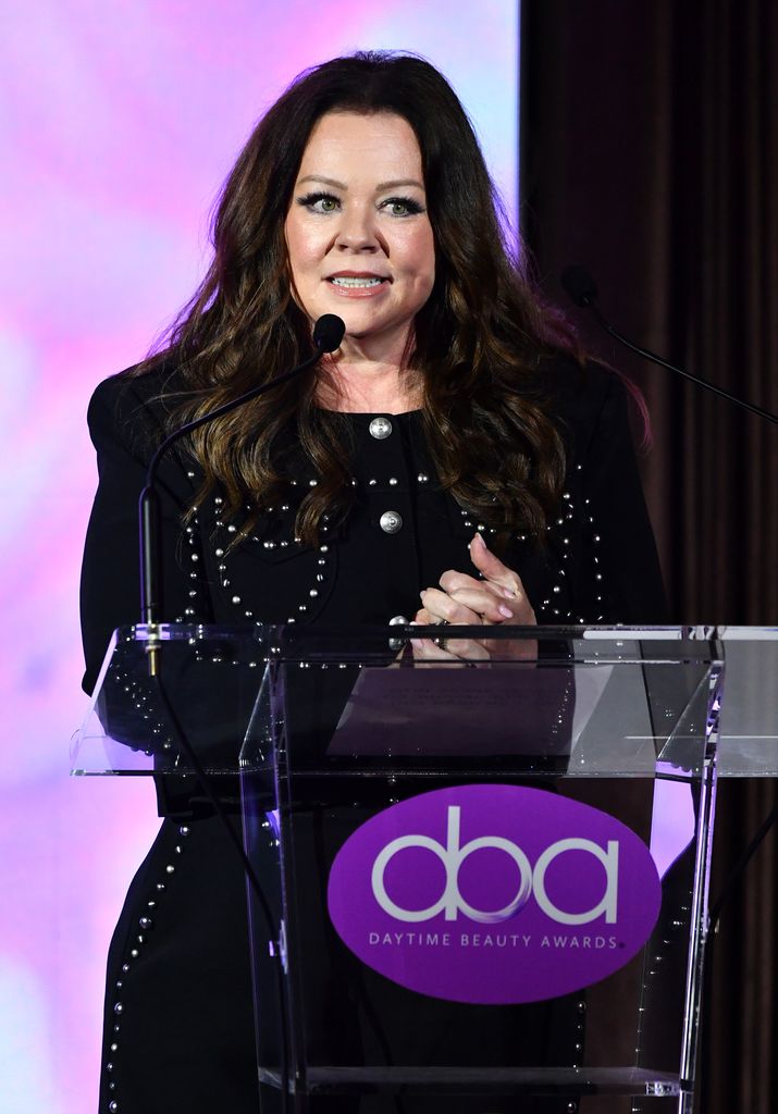 photo of melissa mccarthy speaking into pic at podium on stage