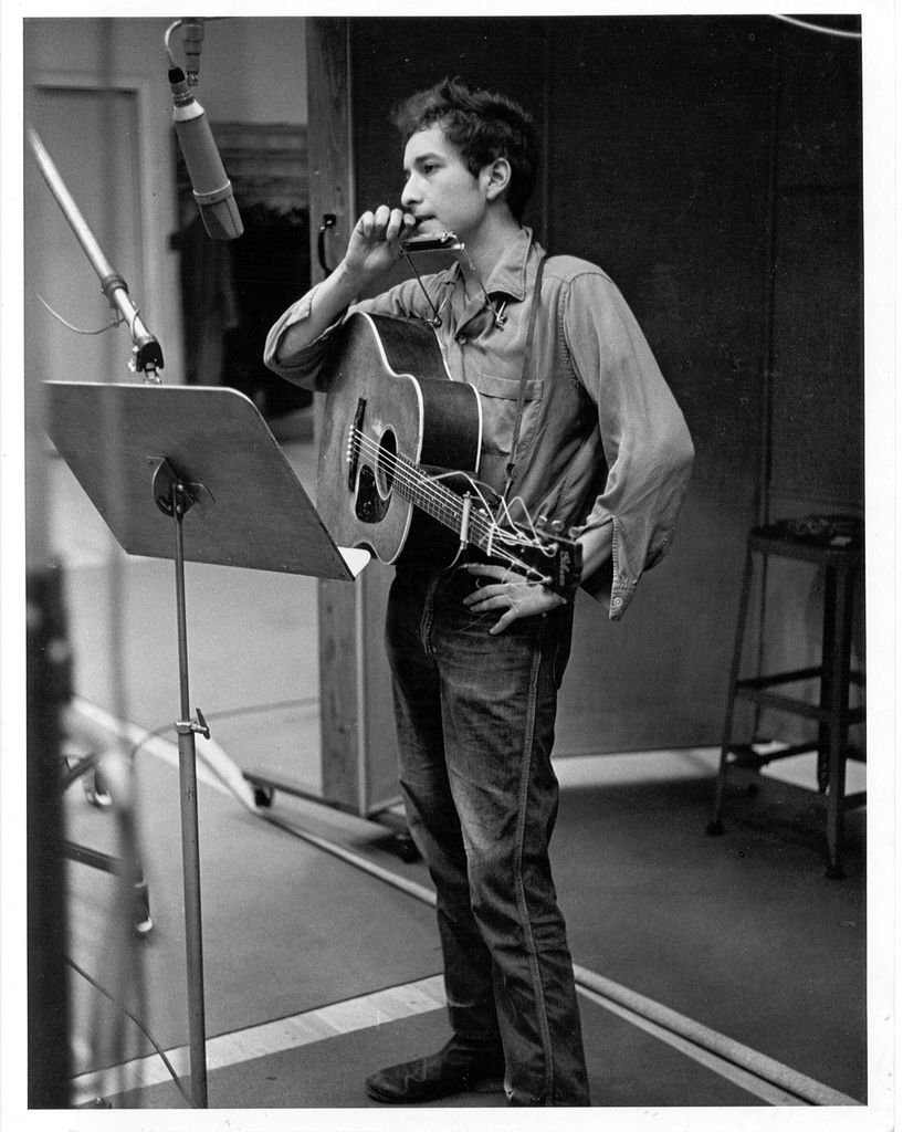 Bob Dylan recording his first album, "Bob Dylan", in front of a microphone with an acoustic Gibson guitar and a harmonica during one of the John Hammond recording sessions in November 1961 at Columbia Studio in New York City, New York.