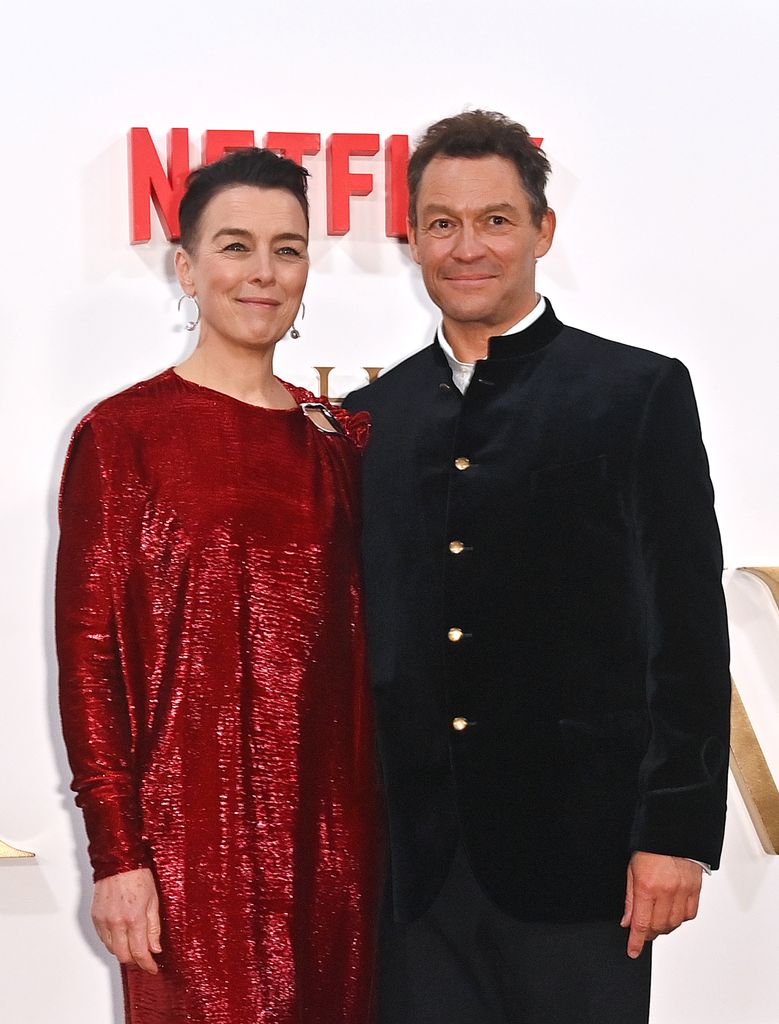 Olivia Williams in a red dress standing with Dominic West in a suit