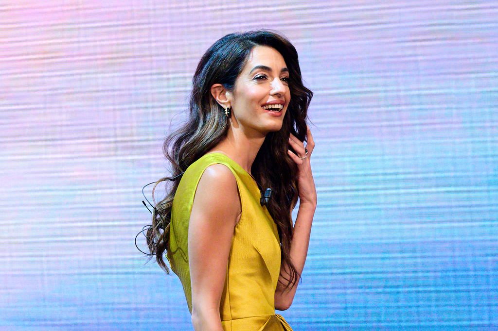 Amal Clooney smiling in a yellow top