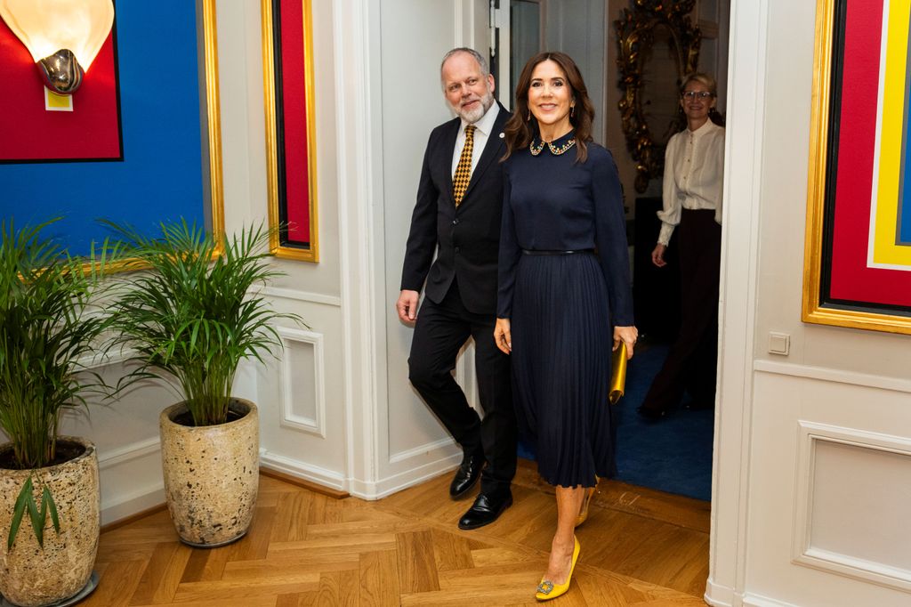 La reine Mary entre dans la chambre en robe bleu marine et talons jaunes