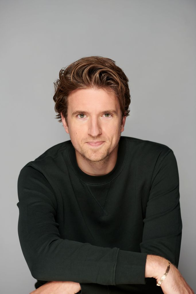 Grey James in a black jumper in front of a grey background