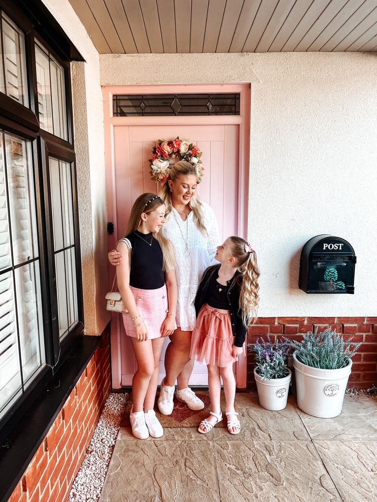 Woman with two daughters smiling in front of a pink door