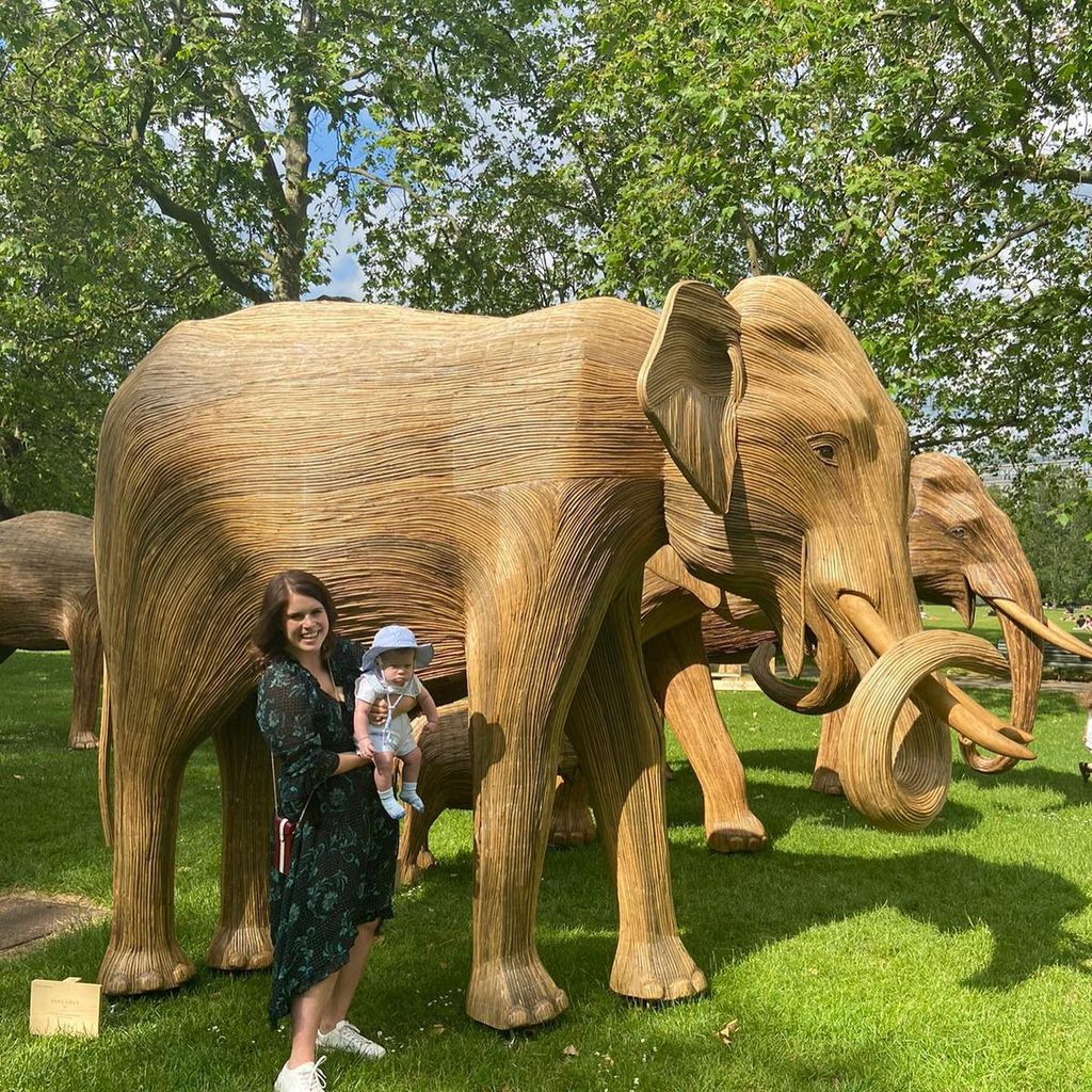 Eugenie and baby August in front of wooden elephant in 2021
