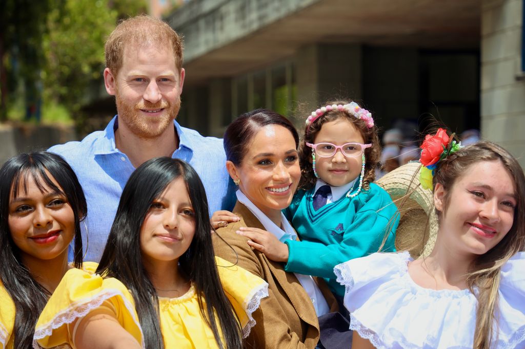 Meghan Markle and Prince Harry with a group of schoolchildren - Meghan is carrying a young girl