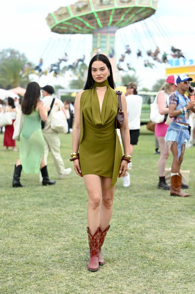 Shanina Shaik wears an olive green mini dress with a cowl neck and red cowboy boots at Coachella.