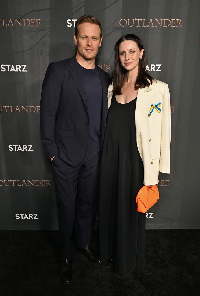 Sam and Caitriona smiling at the camera at an Outlander premiere in 2022