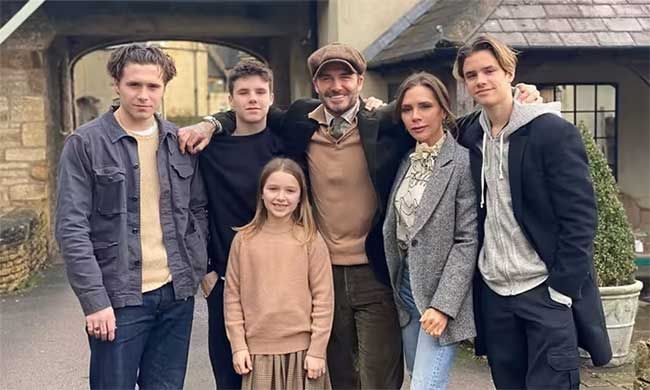 the beckham family comprising of three boys a girl and two parents wear neutral hues as the pose in front of a grand farmhouse style cottage