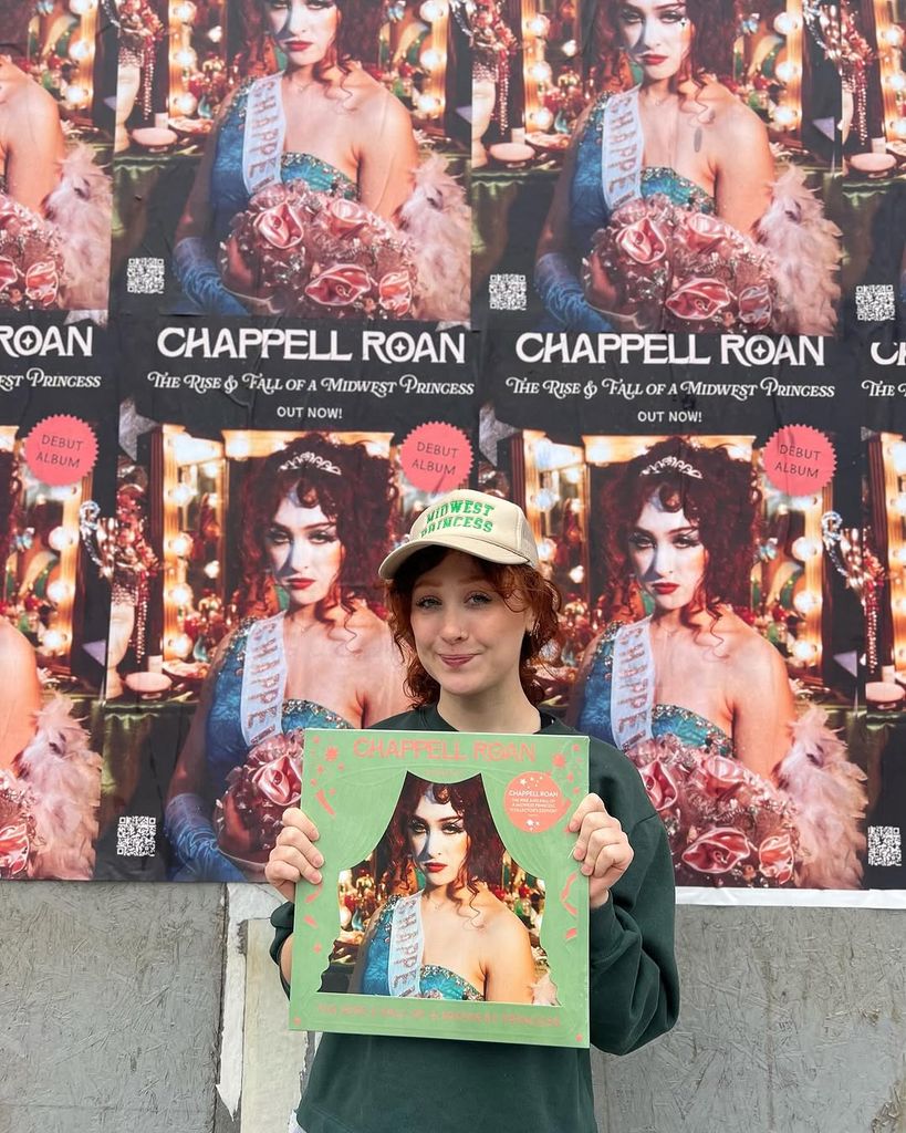 Chappell Roan tenant du vinyle devant ses affiches d'album sur le mur