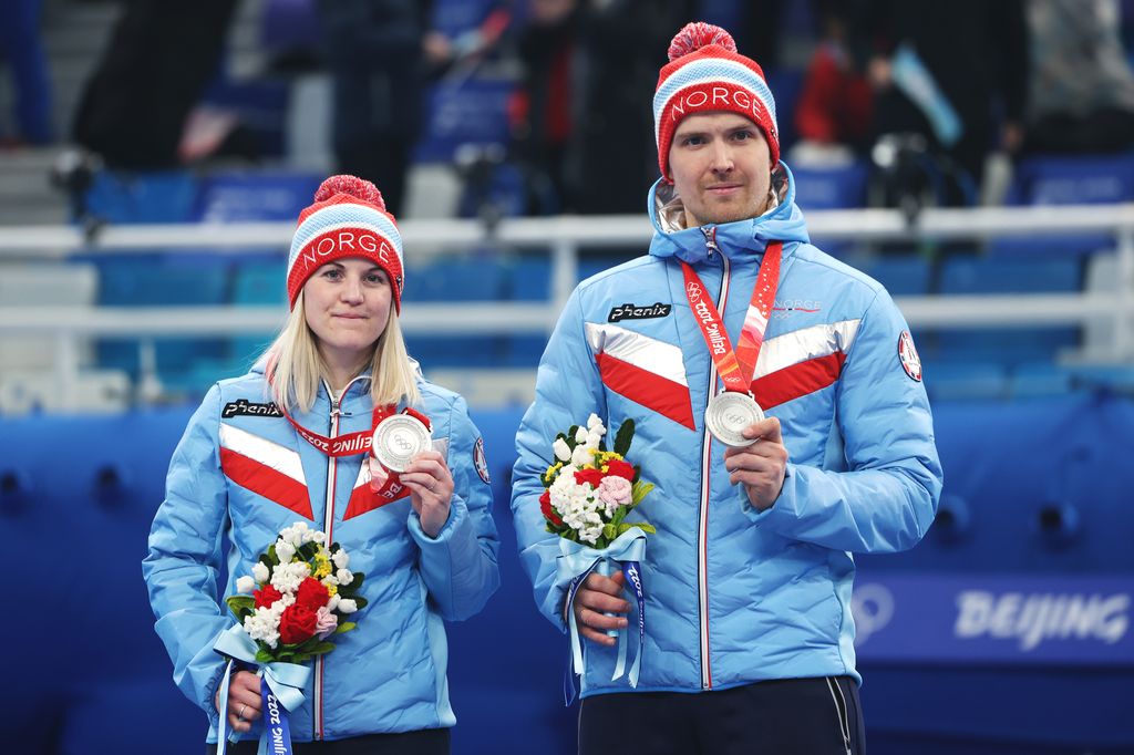 Les médaillés d'argent Kristin Skaslien et Magnus Nedregotten de l'équipe norvégienne posent avec leurs médailles lors de la cérémonie des doubles mixtes de curling. Ils portent des doudounes bleues assorties avec des chapeaux à pompons rouges et bleus et tiennent de petits bouquets de fleurs.